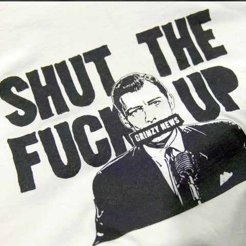 The Collab Tee: Grimzy-STFU from American Lictor features a black and white man in a suit at a microphone with SHUT THE FUCK UP text, mouth covered by a Grimzy News bar. Printed on soft ring-spun cotton. See size guide for best fit.