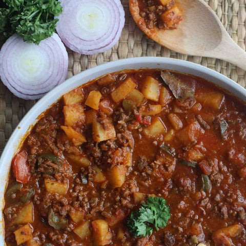 Enjoy a bowl of hearty stew with ground meat, potatoes, and veggies in rich tomato sauce, seasoned with Gustus Vitae’s Slow Cooker Seasonings - 6 Spice Blends Gift Set. Garnished with parsley and served with sliced red onions on the side.