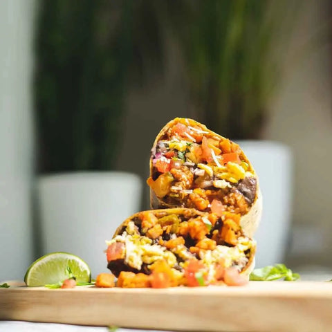 A halved burrito reveals beans, rice, veggies, and cheese—vividly seasoned with Gustus Vitae’s Everything but the Fajita Night Collection—on a wooden board with a lime wedge and green herbs. Set includes 4 gourmet seasonings.