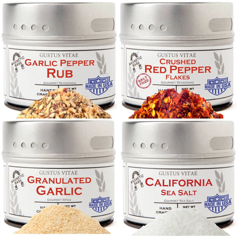 The Gustus Vitae Must Have Kitchen Basics Set of 4 features tins of Garlic Pepper Rub, Crushed Red Pepper Flakes, Granulated Garlic, and California Sea Salt, each attractively displayed with a small pile of seasoning in front.