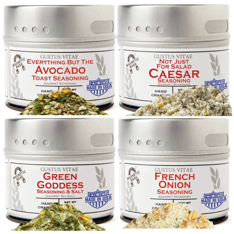 The Gustus Vitae Super Salad Seasonings Collection set of 4 is shown, featuring gourmet blends spilled before each tin: Everything But The Avocado Toast, Not Just For Salad Caesar, Green Goddess Seasoning & Salt, and French Onion Seasoning.