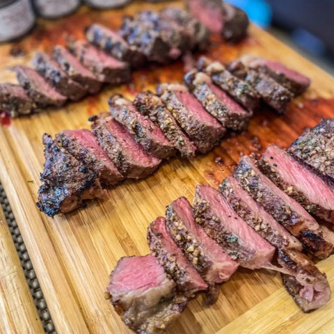 Three rows of sliced, medium-rare steak rest on a wooden board, their juicy pink centers and seared edges glistening with flavorful meat juices and a hint of Gustus Vitae Chefs Secret Luxury Seasonings & Sea Salts Pack.
