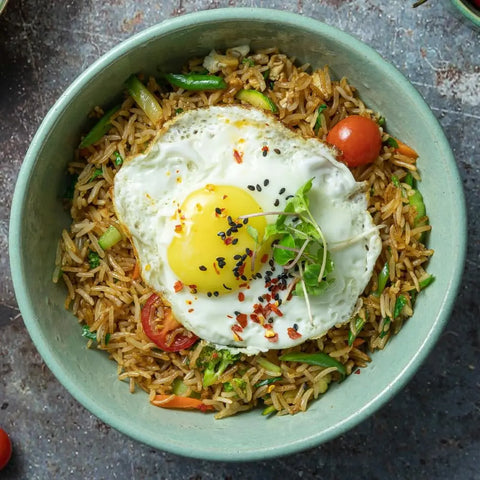 A bowl of fried rice with a sunny-side-up egg, microgreens, black sesame seeds, chili flakes, sliced veggies, and a cherry tomato—all enhanced by Gustus Vitaes Six Elements of Flavor Seasoning Set for rich depth and balanced flavor.