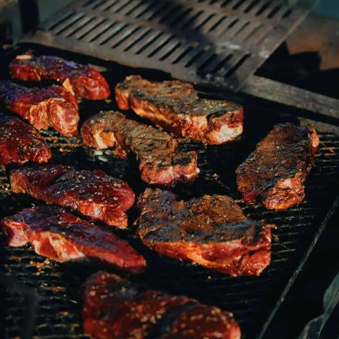 Steaks seasoned with Gustus Vitaes Gourmet BBQ Steak & Beef Seasoning Gift Set - Six Pack are grilling to perfection, showcasing ideal grill marks and varying from rare to medium-rare doneness.