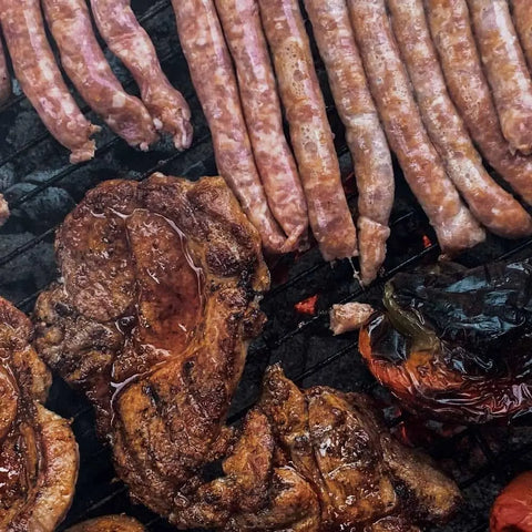 Grilled sausages, pork chops, and bell peppers sizzle over the barbecue, seasoned with Gustus Vitae’s Gourmet BBQ Steak & Beef Seasoning Gift Set – Six Pack, showing perfect grill marks and juicy flavors.