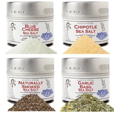The Gustus Vitae Greatest Hits—Essential Summer Sea Salts set includes four tins: Blue Cheese, Chipotle, Naturally Smoked, and Garlic Basil, each displayed with a small pile of its vibrant infused sea salt in front.