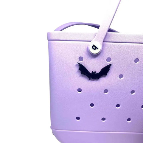 A close-up of a light purple Bogg Bag with small circular holes, featuring the Chatelet Manufacturing BOGLETS Bat Halloween tote bag charm and a handle with a white b button, perfect for adding more Bogg Bag accessories.