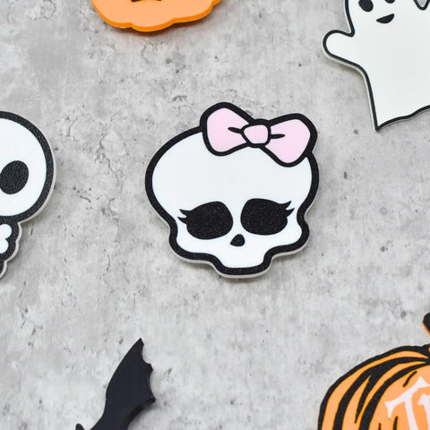 The FRESHe BAGLETS Halloween Cute Pink Bow & Skull Charm by Chatelet Manufacturing features a skull with a pink bow amid pumpkins, ghosts, and skeletons—perfect for any rubber tote bag. Made in the USA.