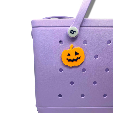A light purple Bogg Bags tote features circular holes and a Chatelet Manufacturing BOGLETS Jack O Lantern Halloween Tote Bag Charm, with its handle secured by a white button bearing a lowercase “b.”.