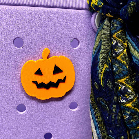 A BOGLETS - Halloween Tote Bag Charm (Jack O Lantern) by Chatelet Manufacturing is attached to a purple shoe with holes, next to a blue patterned scarf tied onto the shoe.
