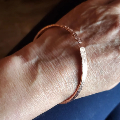 A close-up of a hand wearing an Alexa Martha Designs Stackable Hammered Double Canted Angle Bangle on the wrist, set against a dark background.