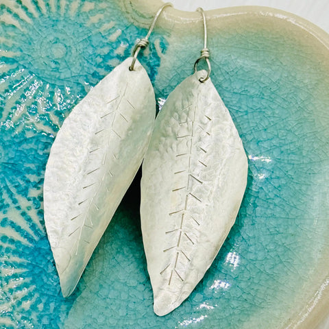 JANECKA Sterling Silver Hand Forged Leaf Earrings by Janecka, featuring etched vein details, displayed on a textured turquoise ceramic dish.