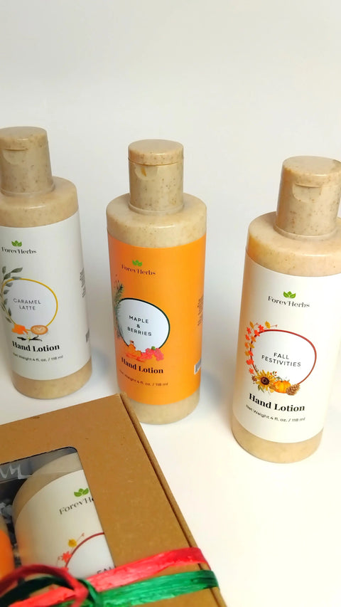 Three bottles of Forev'Herbs Hand Lotion Gift Set—Caramel Latte, Maple Berries, and Fall Festivities—stand upright on a white surface with a box partly visible in the lower left. The perfect seasonal gift set for hydrated hands.