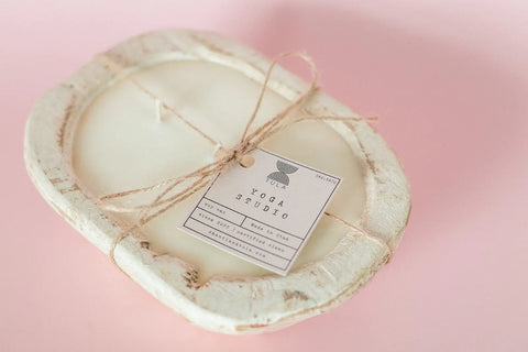 Add a rustic touch with Shanti + Tulas Hand-Poured Soy Dough Bowl Candle – Oval 3-Wick, available in antique white. Made in the USA, its shown here holding a YOGA STUDIO card on a light pink background.