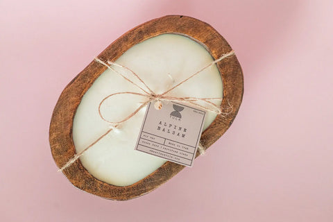 The Shanti + Tula Hand-Poured Soy Dough Bowl Candle, an oval 3-wick in rustic or antique white, sits on a light pink background tied with twine and an “Alpine Balsam” label for a charming touch. Made in the USA.