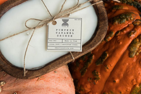 A Hand-Poured Soy Dough Bowl Candle – Oval 3-Wick by Shanti + Tula, in rustic or antique white, sits tied with twine between two textured pumpkins—one orange and bumpy, one light orange and smooth—for a cozy autumn accent.