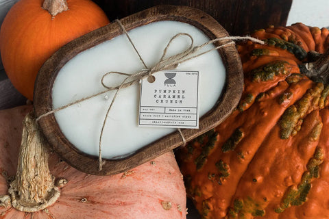 The Shanti + Tula Hand-Poured Soy Dough Bowl Candle—Oval 3-Wick, shown in Pumpkin Caramel Crunch, sits among pumpkins. Tied with twine, this 100% soy wax candle adds rustic autumn charm. Made in the USA; available in Rustic & Antique White.