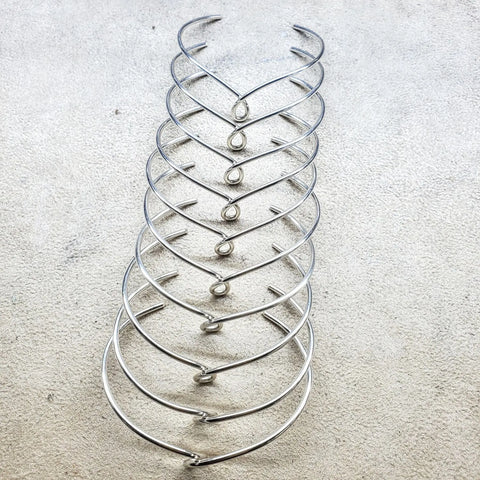 Nine Timeless Classic Silver Reversible Teardrop Awareness Bangles by Alexa Martha Designs are arranged in a neat vertical row on a textured light gray surface, each reflecting the elegance of handcrafted jewelry.