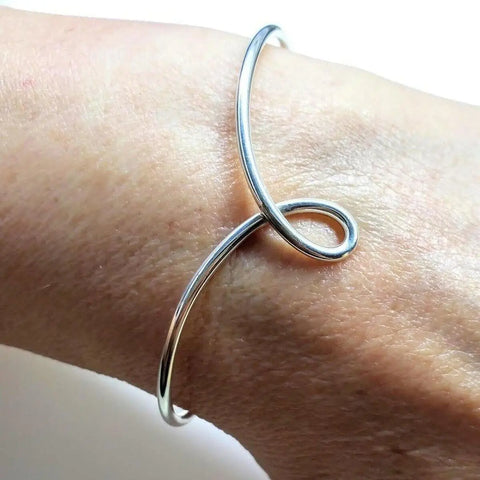 The Timeless Classic Silver Reversible Teardrop Awareness Bangle by Alexa Martha Designs is shown on a wrist—an elegant, handcrafted sterling silver piece with a unique looped design.