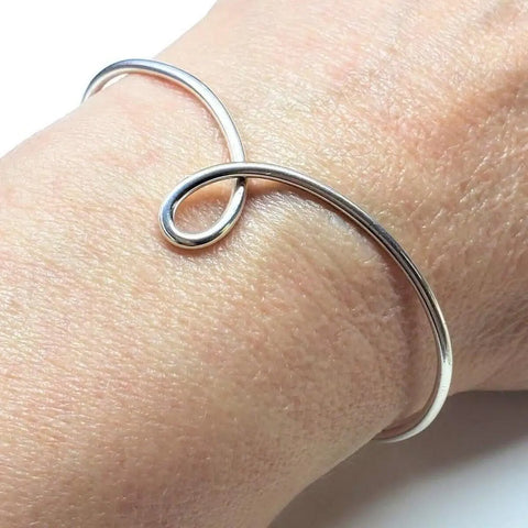 The Timeless Classic Silver Reversible Teardrop Awareness Bangle by Alexa Martha Designs rests gracefully on light-toned skin, its sleek sterling silver and minimalist, handcrafted design adding an elegant touch to the wrist.
