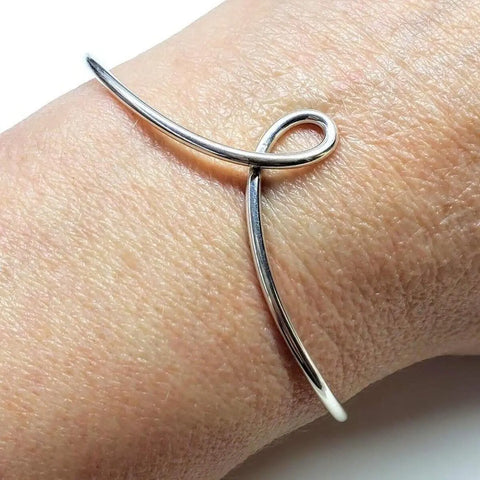 The Timeless Classic Silver Reversible Teardrop Awareness Bangle by Alexa Martha Designs, featuring a minimalist looped design, is a striking handcrafted sterling silver piece worn elegantly on the wrist.