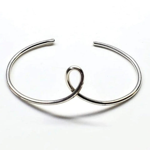 The Timeless Classic Silver Reversible Teardrop Awareness Bangle by Alexa Martha Designs features a minimalist open-ended design with a central loop, beautifully presented on a white background.