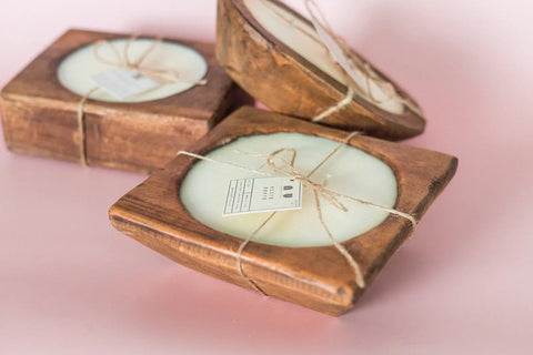 Three Shanti + Tula Handcrafted 3-Wick Square Dough Bowl Candles—soy wax, natural & antique white finish—are tied with twine and labeled, arranged on a soft pink surface, reflecting eco-conscious USA craftsmanship.