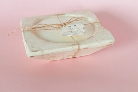 The Shanti + Tula Handcrafted 3-Wick Square Dough Bowl Candle features soy wax in a natural & antique white finish—an eco-conscious, elegant piece made in the USA, showcasing artisanal craftsmanship against a soft pink backdrop.