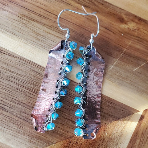 Blue Green Hammered Copper Bar Crystal Earrings by Alexa Martha Designs feature hammered copper plates with blue beads along one edge, shown on a wooden surface.
