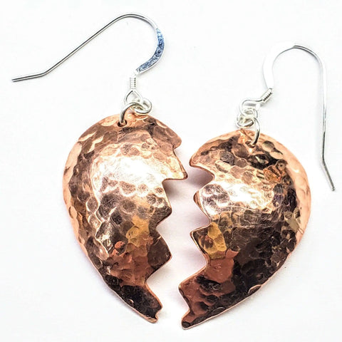 The Broken Heart Earrings From Sculpted Copper by Alexa Martha Designs feature two hammered copper halves with jagged inner edges, forming a unique heart design—shown on a white background.