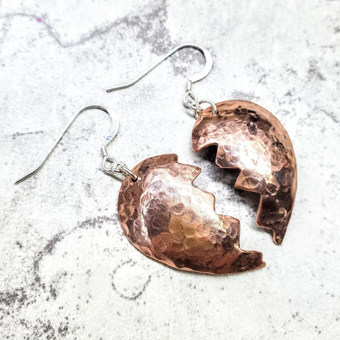 Broken Heart Earrings from Sculpted Copper by Alexa Martha Designs feature two jagged halves crafted from hammered copper, shown on a light textured background.