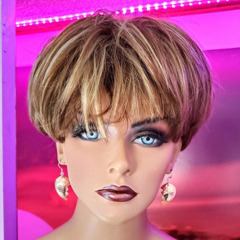 A mannequin head with short, layered blonde hair and bold makeup wears Alexa Martha Designs Broken Heart Earrings from sculpted copper, set against a pink and purple LED-lit background.
