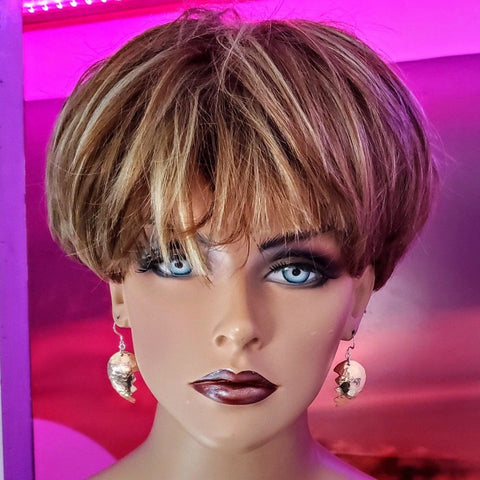 A mannequin head with short, layered light brown hair, bold makeup, and dark lipstick models Alexa Martha Designs Broken Heart Earrings from Sculpted Copper, set against a pink and purple-lit background for a striking look.
