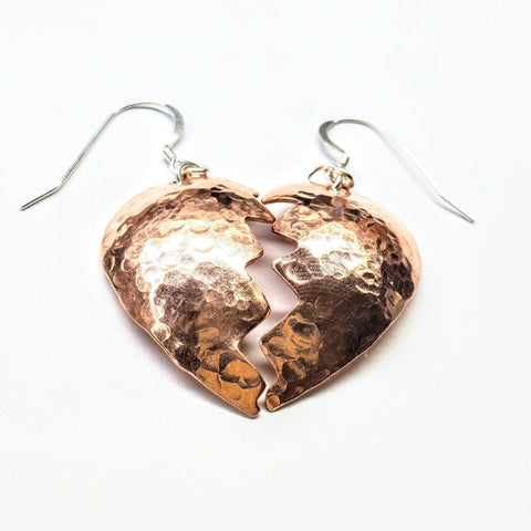 Broken Heart Earrings from Sculpted Copper by Alexa Martha Designs feature a unique design of two hammered copper halves with silver hooks, displayed on a white background.