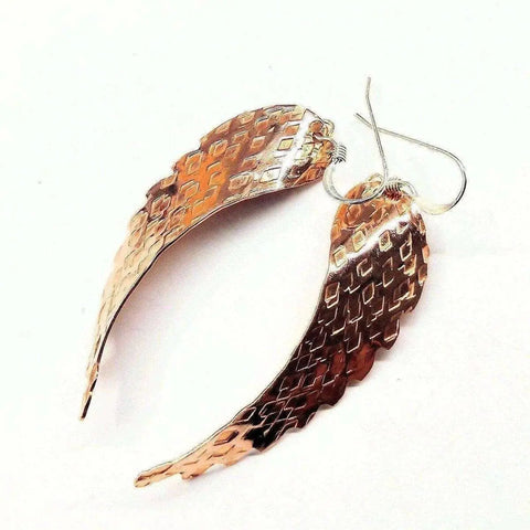 Copper Hammer Pattern Sculpted Angel Wings Earrings by Alexa Martha Designs feature handcrafted, copper-toned wings with a textured scale-like pattern and hook fastenings, shown on a white background.