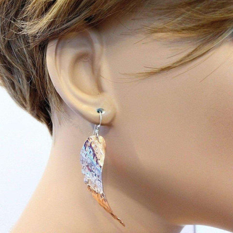 A close-up of a mannequin’s ear wearing Alexa Martha Designs’ Copper Hammer Pattern Sculpted Angel Wings Earrings, with short brown hair partially visible.