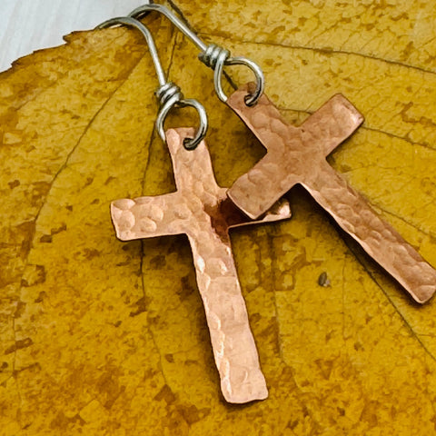 JANECKA Copper Cross Earrings by Janecka, hand forged with sterling silver ear wires, shown on a yellow autumn leaf.