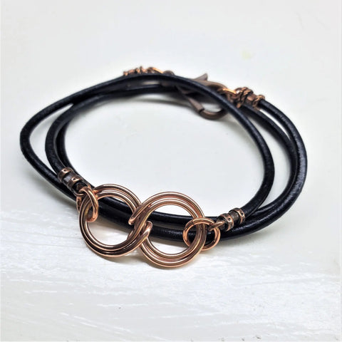 The Alexa Martha Designs Copper Double Infinity Gender Neutral Leather Wrap Bracelet features a black leather band with a copper double infinity centerpiece and matching clasps, adding modern elegance to any style.