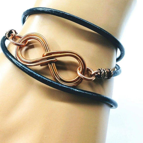The Copper Double Infinity Gender Neutral Leather Wrap Bracelet by Alexa Martha Designs is shown on a wrist, looping several times with its metallic infinity symbol charm displayed at the center.