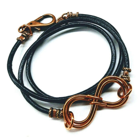 The Copper Double Infinity Gender Neutral Leather Wrap Bracelet by Alexa Martha Designs is displayed on a white background, featuring a black leather band and copper double infinity charm with a matching clasp.