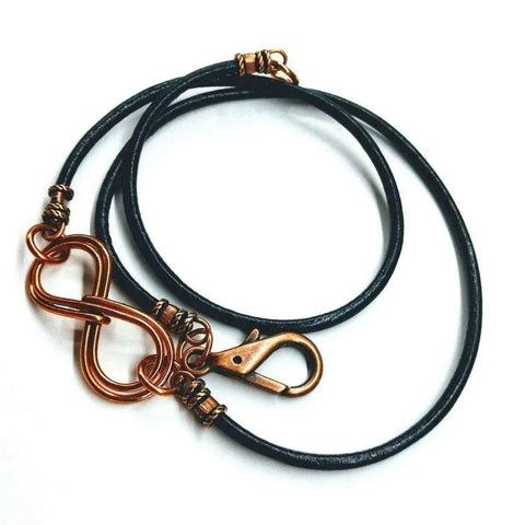 The Copper Double Infinity Gender Neutral Leather Wrap Bracelet by Alexa Martha Designs features black leather, a copper lobster clasp, and a double infinity pendant, shown on a white background.