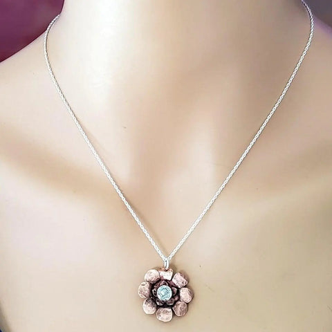 Handmade in Montana, the Copper Crystal Flower Blossom Spinner Necklace by Alexa Martha Designs features a flower pendant with pink petals and a light blue center, elegantly displayed on a mannequin bust.