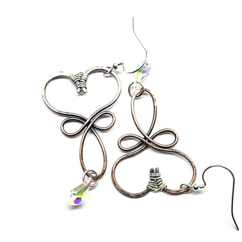 The Crystal Drop Copper Heart Earrings by Alexa Martha Designs feature heart-shaped copper wire with iridescent Swarovski crystals, handmade with intricate loops. These sparkling earrings are displayed on a white background.