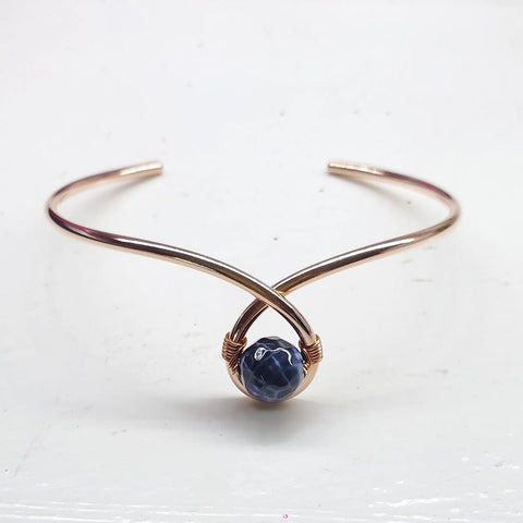 The Alexa Martha Designs Handmade Copper Ribbon Child Abuse Awareness Teardrop Bangle is shown on a white surface, featuring a minimalist teardrop shape with a copper ribbon centerpiece.