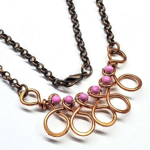 The Copper Wire Wrapped Sculpted Pink Gemstone Necklace by Alexa Martha Designs features a dark metal chain, five gold-tone loops with pink beads, and a lobster clasp for closure.