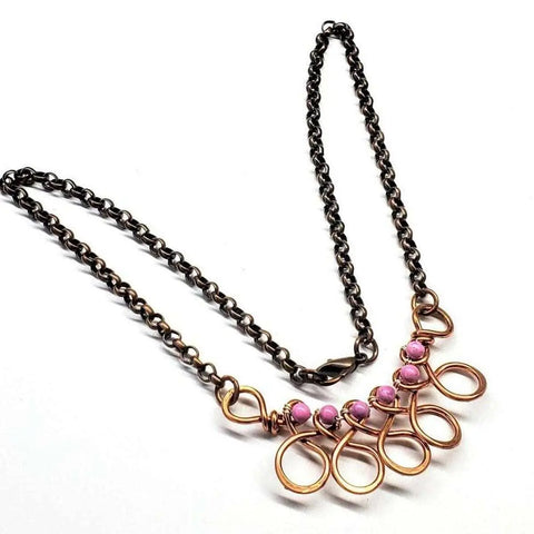 The Copper Wire Wrapped Sculpted Pink Gemstone Necklace by Alexa Martha Designs features four pink gemstones on copper loops, showcasing an artisan, handcrafted statement design against a white background.