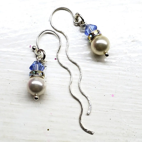 Alexa Martha Designs Ergonomic Crystal Pearl Wavy Ear Threaders feature sterling silver with wavy hooks, each adorned with a white pearl and faceted light blue crystal bead against a white background.