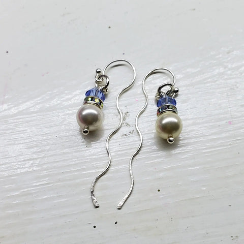 A pair of Ergonomic Crystal Pearl Wavy Ear Threaders by Alexa Martha Designs, featuring wavy sterling silver hooks with round white pearls, blue Swarovski crystals, and silver accents, displayed on a white surface.