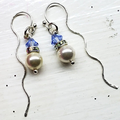The Ergonomic Crystal Pearl Wavy Ear Threaders by Alexa Martha Designs feature white pearls, blue crystal beads, and silver accents on wavy sterling silver hooks, shown on a white textured surface.
