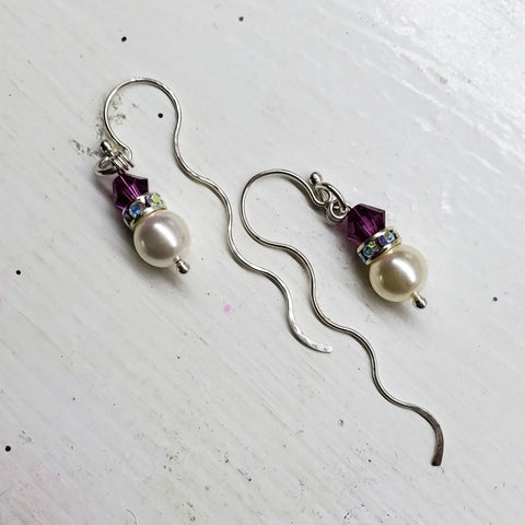Ergonomic Crystal Pearl Wavy Ear Threaders by Alexa Martha Designs feature wavy sterling silver hooks, a purple crystal bead, clear rhinestones, and an off-white pearl, beautifully displayed on a white surface.